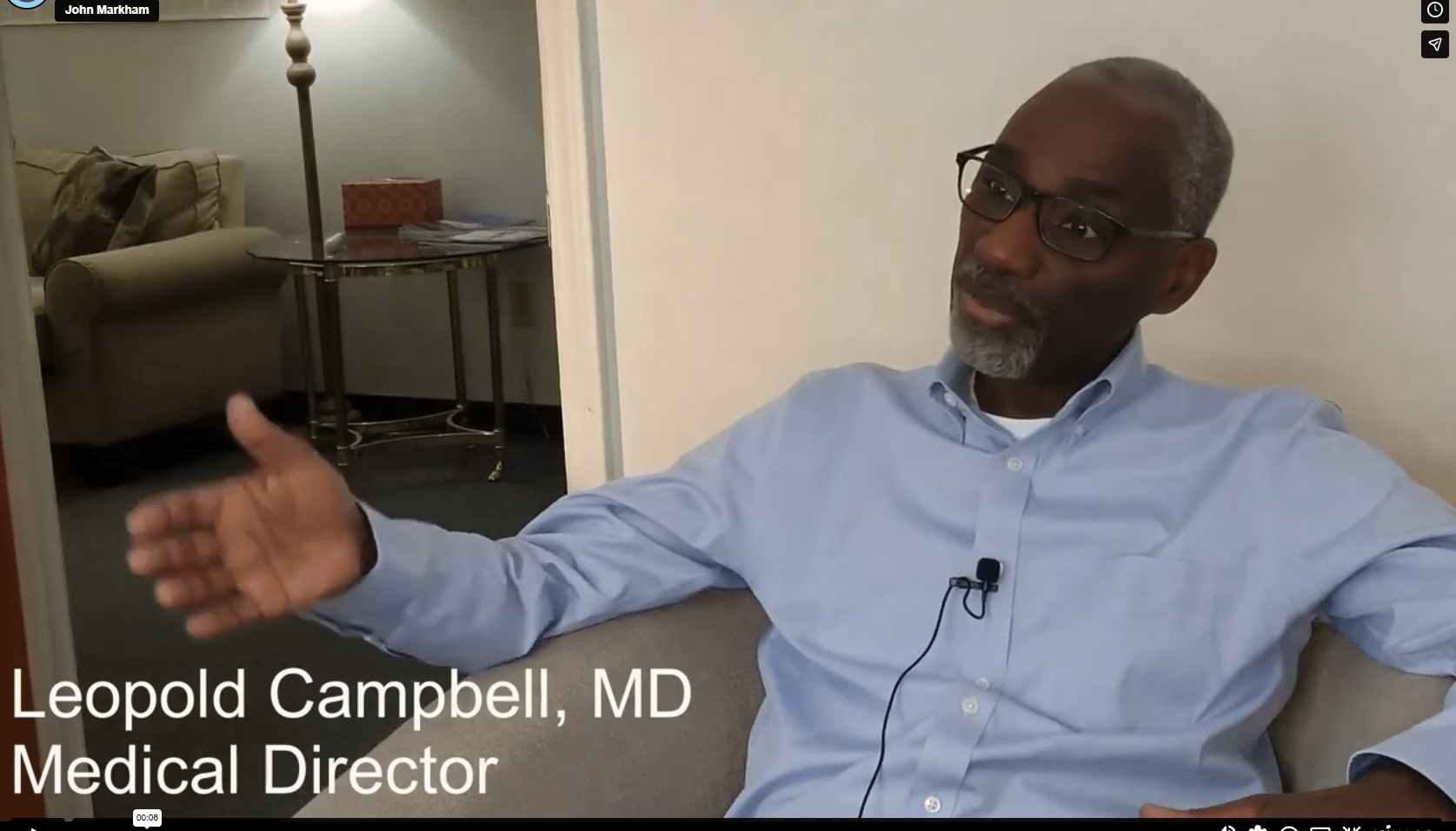 Man with glasses and gray hair wearing a light blue shirt speaks in an interview; on-screen caption reads Leopold Campbell, MD, Medical Director.